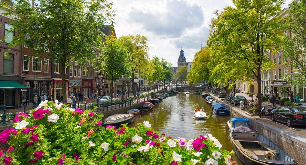 Scenic Amsterdam canal with colorful blooming flowers on a bridge, perfect setting for an amsterdam hen do.