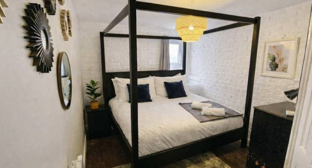 Double four-poster bed and white brick feature wall at the Bournemouth Hot Tub Garden hen party house.