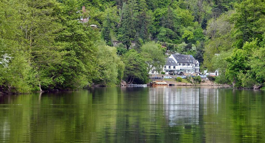 Scenic view along River Wye with lush green woodland hills, tranquil countryside backdrop for a Herefordshire hen do.
