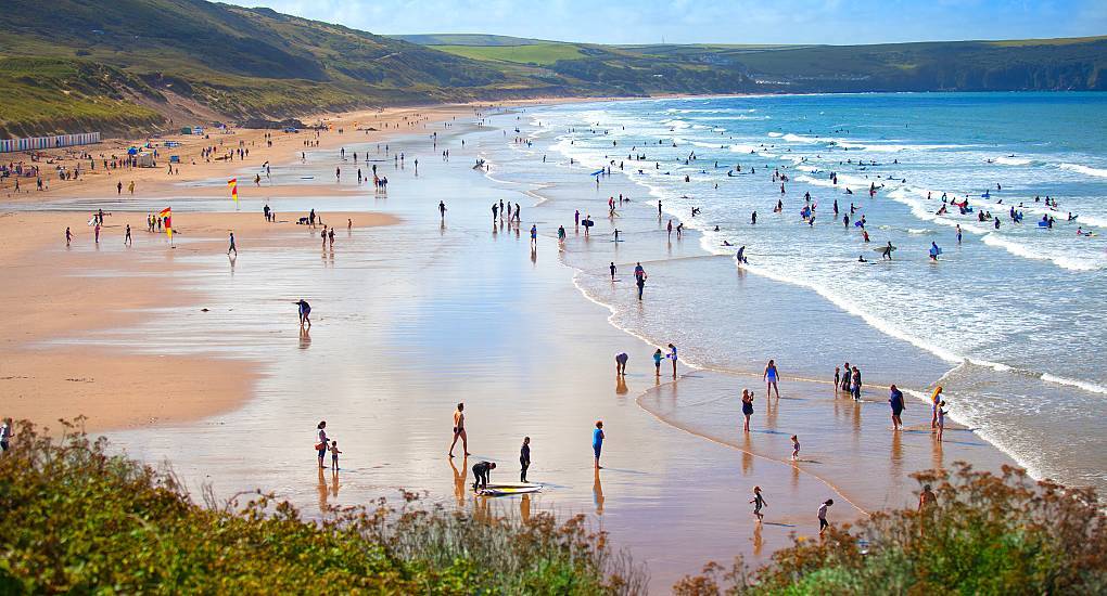 Crowds and surfers enjoying golden sand and waves at Woolacombe Beach, sunny coastal setting for a Woolacombe stag do.